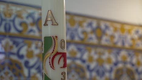 paschal candle in church setting, decorative tilework and engraved ceramic details