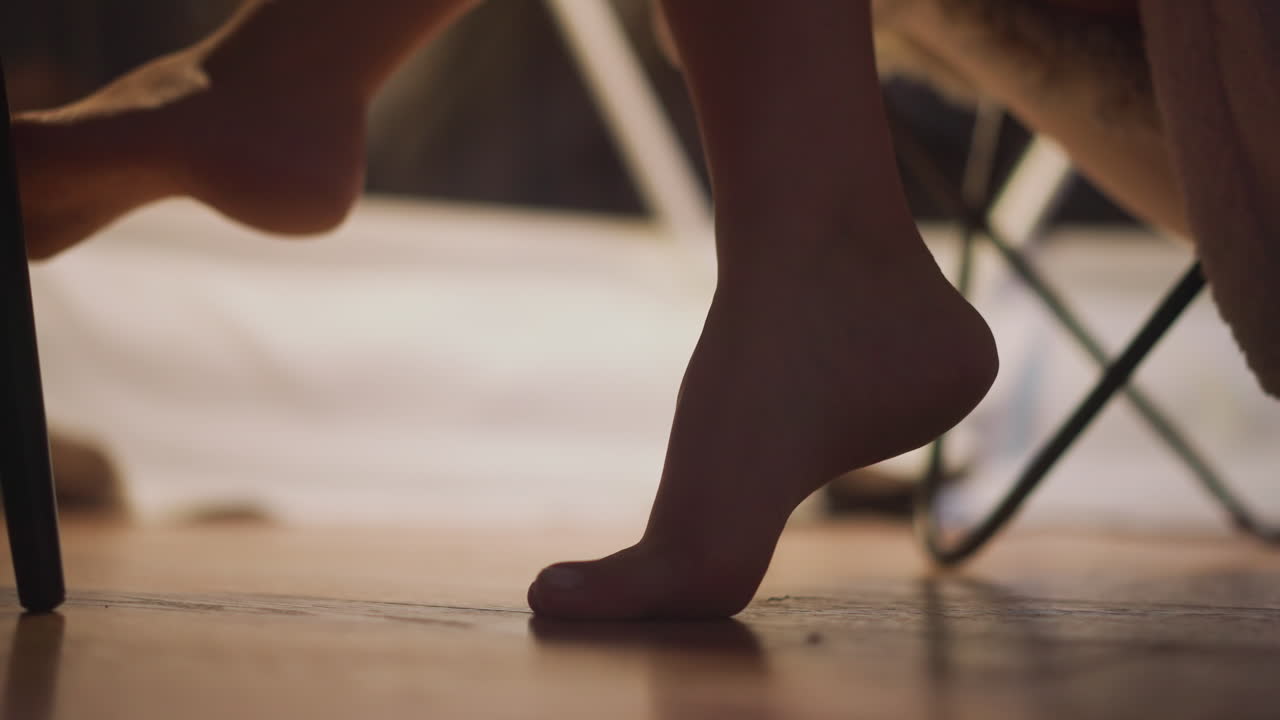 발 벗은 여자가 관광 호텔 방에서 의자에서 휴식을 취하고 있습니다. 저녁에 평온하고 편안한 분위기를 즐기고 있습니다. 여성 몸의 팔다리 느린 모션