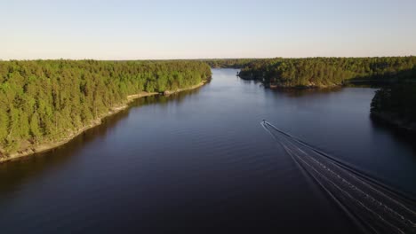 Aerial-view-following-a-boat,-driving-in-the-Swedish-archipelago,-golden-hour,-in-Sweden