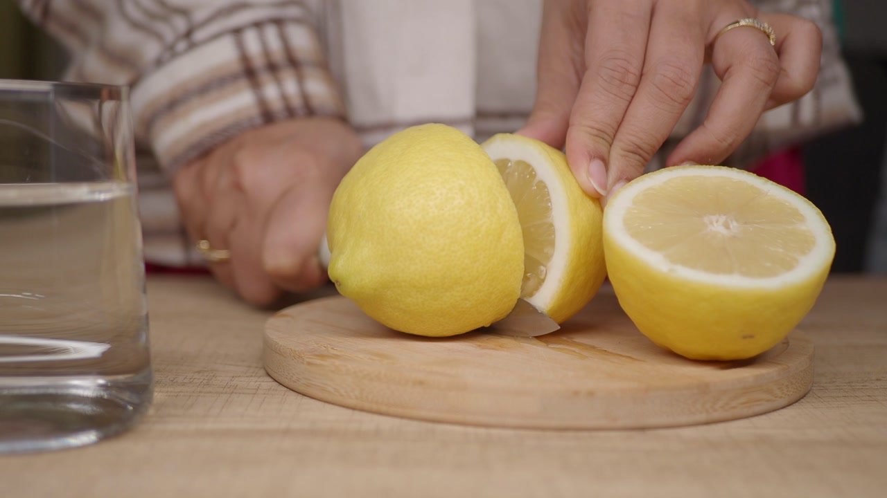 Close-up of Hands Cutting a Fresh Lemon on a Wooden Board