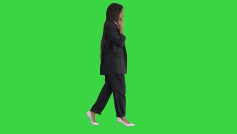 casual african american businesswoman talking on phone while walking on a green screen, chroma key