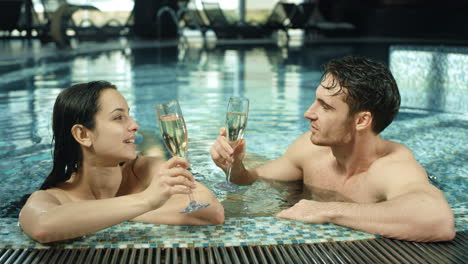 Beautiful-couple-clinking-glasses-in-spa-pool.-Man-and-woman-flirting-in-jacuzzi