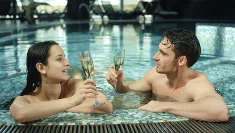 hermosa pareja tintineando vasos en la piscina del spa. hombre y mujer coqueteando en el jacuzzi