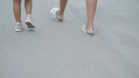 a pregnant woman and her young daughter, dressed in light summer outfits, walk hand-in-hand along a street in a residential neighborhood. the daughter holds a toy, enjoying the peaceful moment outdoor