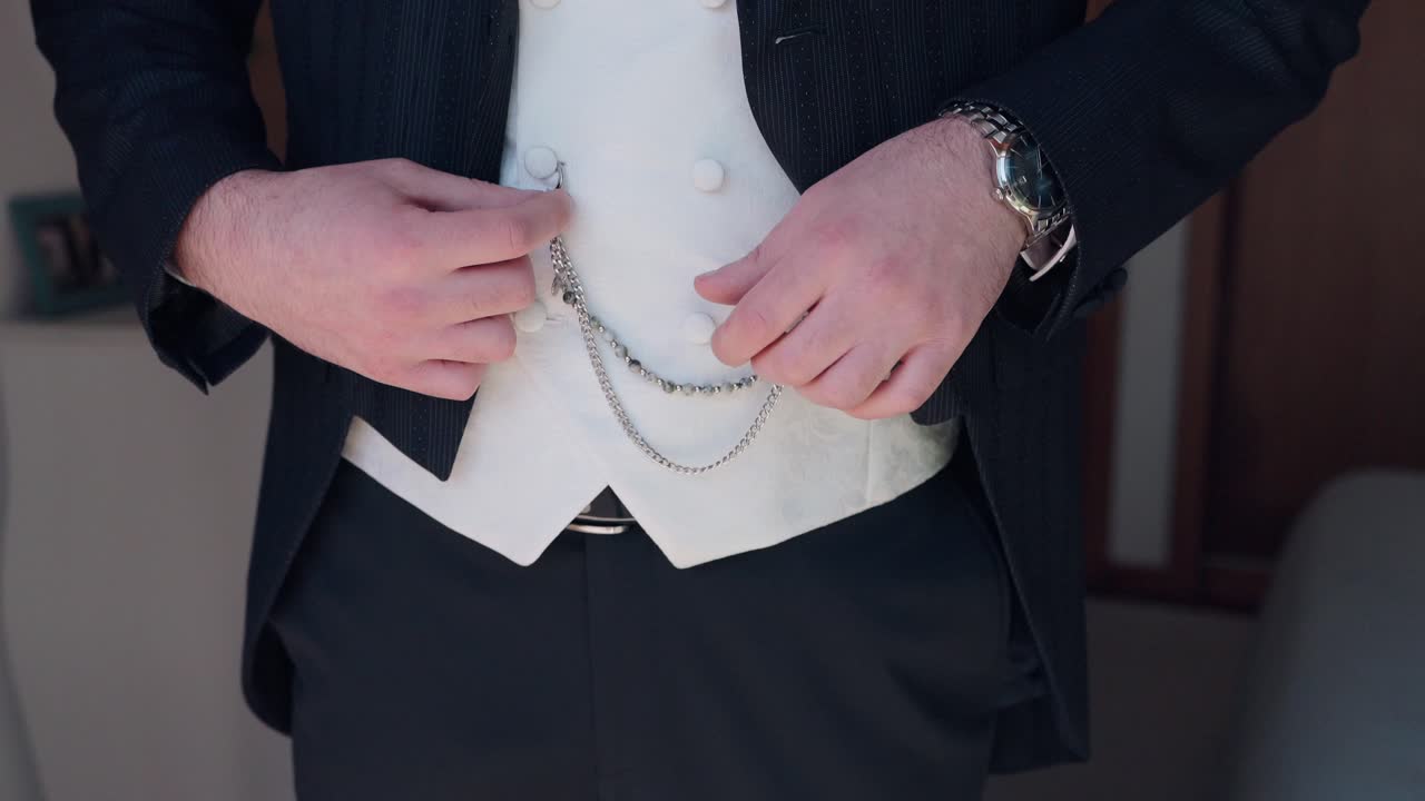 man fastens decorative chain on vest while getting dressed for formal event