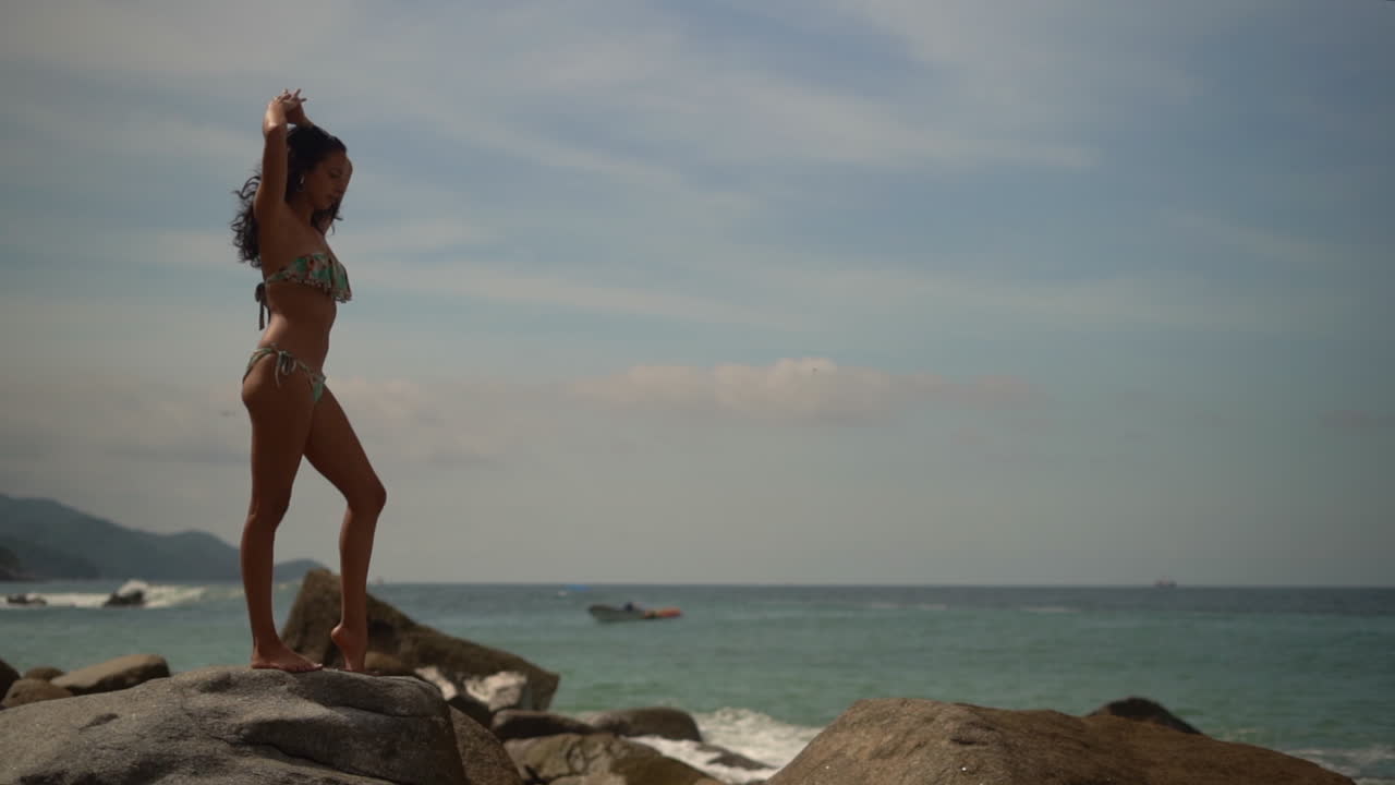 Bella giovane donna in bikini su una spiaggia rocciosa che si sta allungando sotto il sole - rallentatore