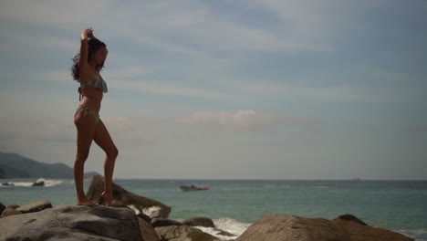 Beautiful-young-woman-in-a-bikini-on-rocky-beach-stretching-in-the-sunshine---slow-motion