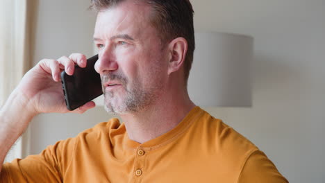 Senior man talking on smartphone at home, wearing casual orange shirt
