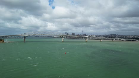 Puente-Del-Puerto-De-Auckland-Con-Vistas-Al-Puerto-Turquesa-De-Waitemata-Y-Al-Horizonte-Del-Centro-De-La-Ciudad-Desde-Un-Dron-Aéreo-Que-Recorre-Las-Aguas-En-Nueva-Zelanda