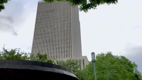 from the gardens in a park, tilting up to reveal a tall, modern highrise office or appartment building