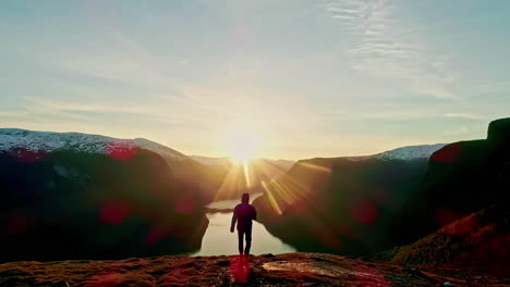 man walks towards the sunset skyline mountain range lake drone shot from behind