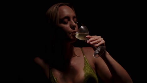 beautiful portrait of an attractive woman enjoying a glass of white wine while wearing an enticing bra in a dark room