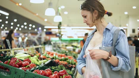 shopping. woman choosing bio red bell pepper in vegetable store or supermarket. takes one by one and puts it in a cellophane bag. red freshsweet peppers