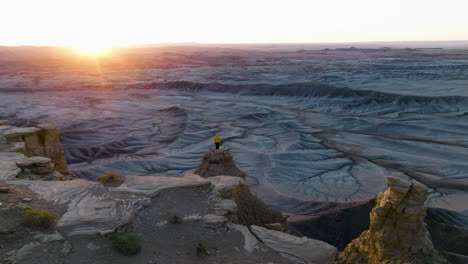 adventurous girl wearing yellow jacket, admiring beautiful sunrise while standing on dangerous edge of abrupt canyon in utah, usa