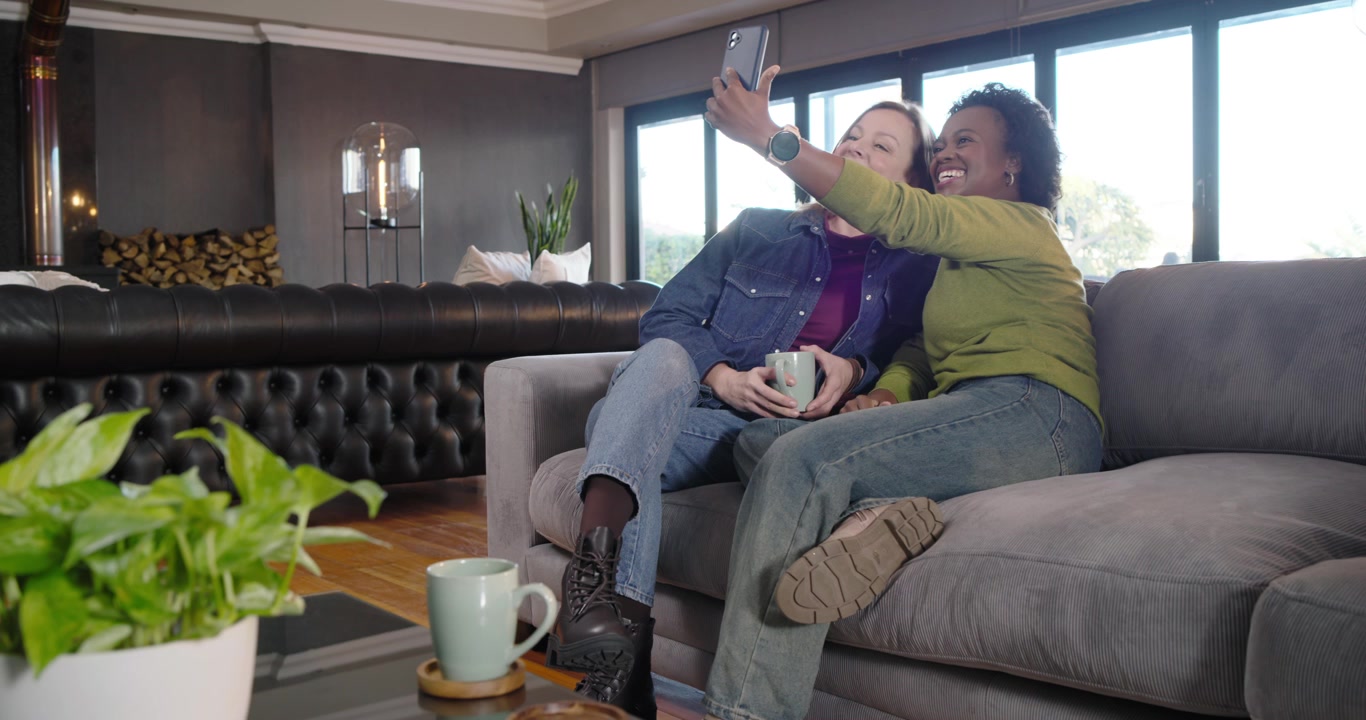 Diverse amiche mostrano il telefono, ridono, appoggiate al divano, scattando un selfie per immortalare il momento