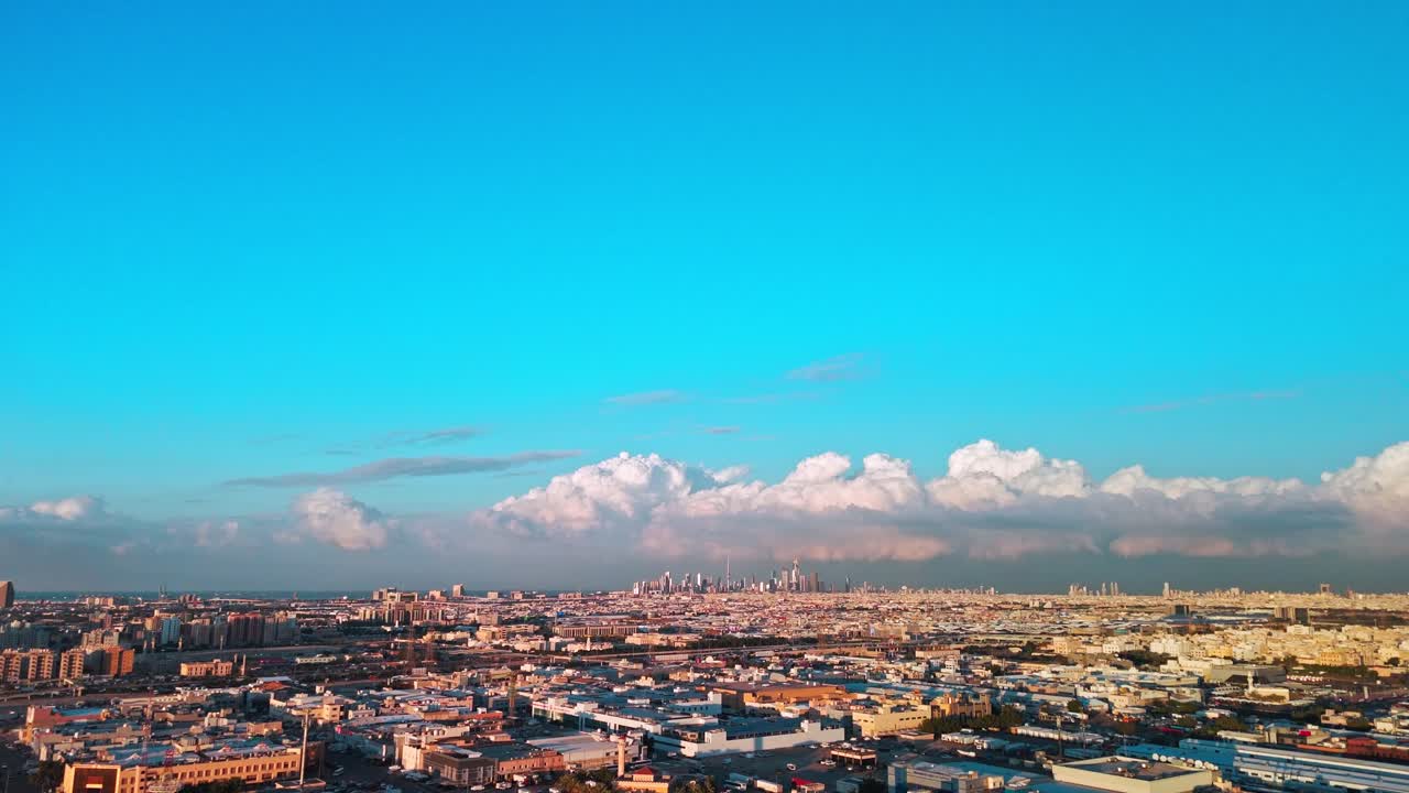 Bredt panorama over Kuwait City med en stor, blå himmel og en række bløde cumulusskyer. Fjerntliggende downtown skyline over spredte forstæder, klart eftermiddagslys, der er ideelt til rejsereportager og etablerende billeder.