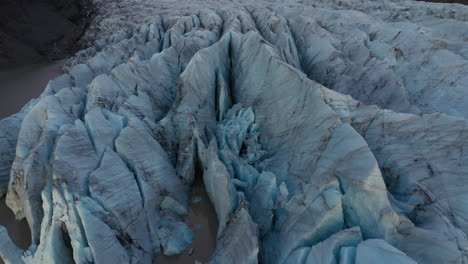 Dramatic-aerial-glacier-reveal-during-blue-hour-with-mountain-peaks-and-blue-ice