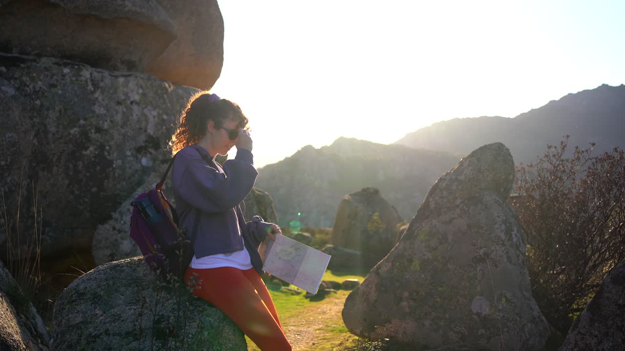 mujer joven alegre leyendo un mapa en medio de formaciones rocosas durante un viaje de senderismo