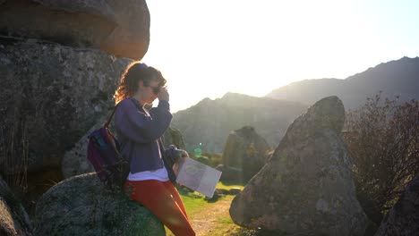 Cheerful-young-woman-reading-map-amidst-rocky-formations-during-hiking-trip