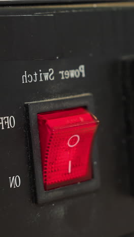 una vista de cerca de la mano con guantes de un técnico presionando el interruptor de energía rojo en un dispositivo de control de temperatura negra