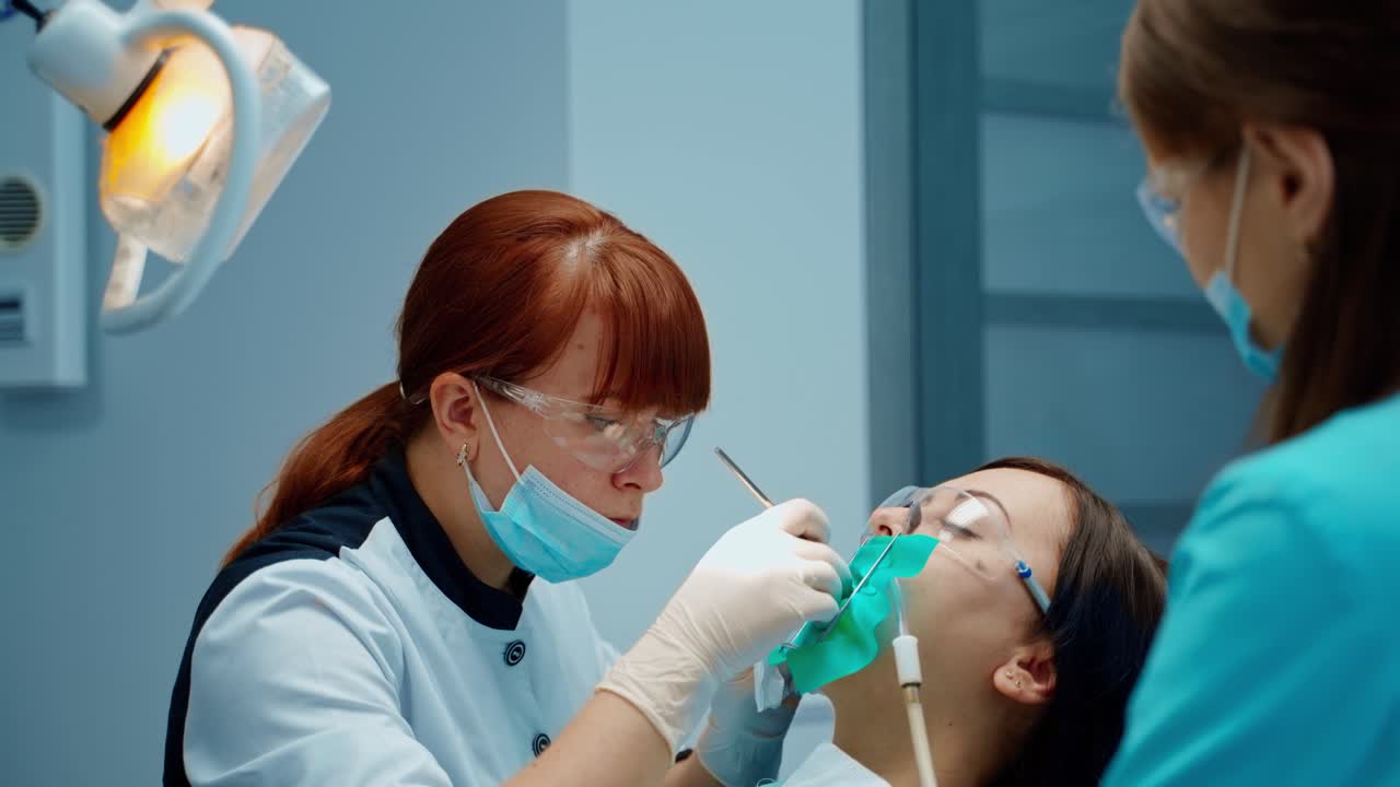 Dentist woman cures patient's tooth attentively. Dental oral hygiene procedure in stomatology clinic. Female stomatologist and a nurse treating girl's teeth.