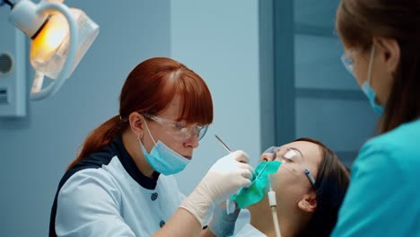 Dentist woman cures patient's tooth attentively. Dental oral hygiene procedure in stomatology clinic. Female stomatologist and a nurse treating girl's teeth.