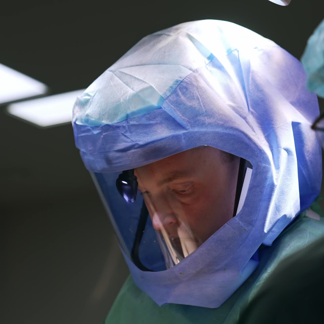 Caucasian male doctor in special protective mask with headlight. Focused surgeon working in a team