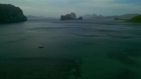 Hilly-green-islands,-boat-and-colorful-water-in-Philippines,-wide-forward-aerial