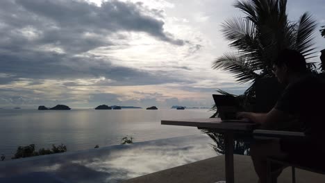 asian man working on the laptop by the pool - panning view