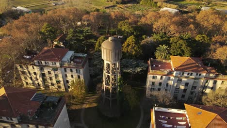 Toma-De-órbita-Aérea-Del-Antiguo-Tanque-De-Agua-De-Hormigón-Durante-La-Puesta-De-Sol-En-El-área-Suburbana,-Argentina