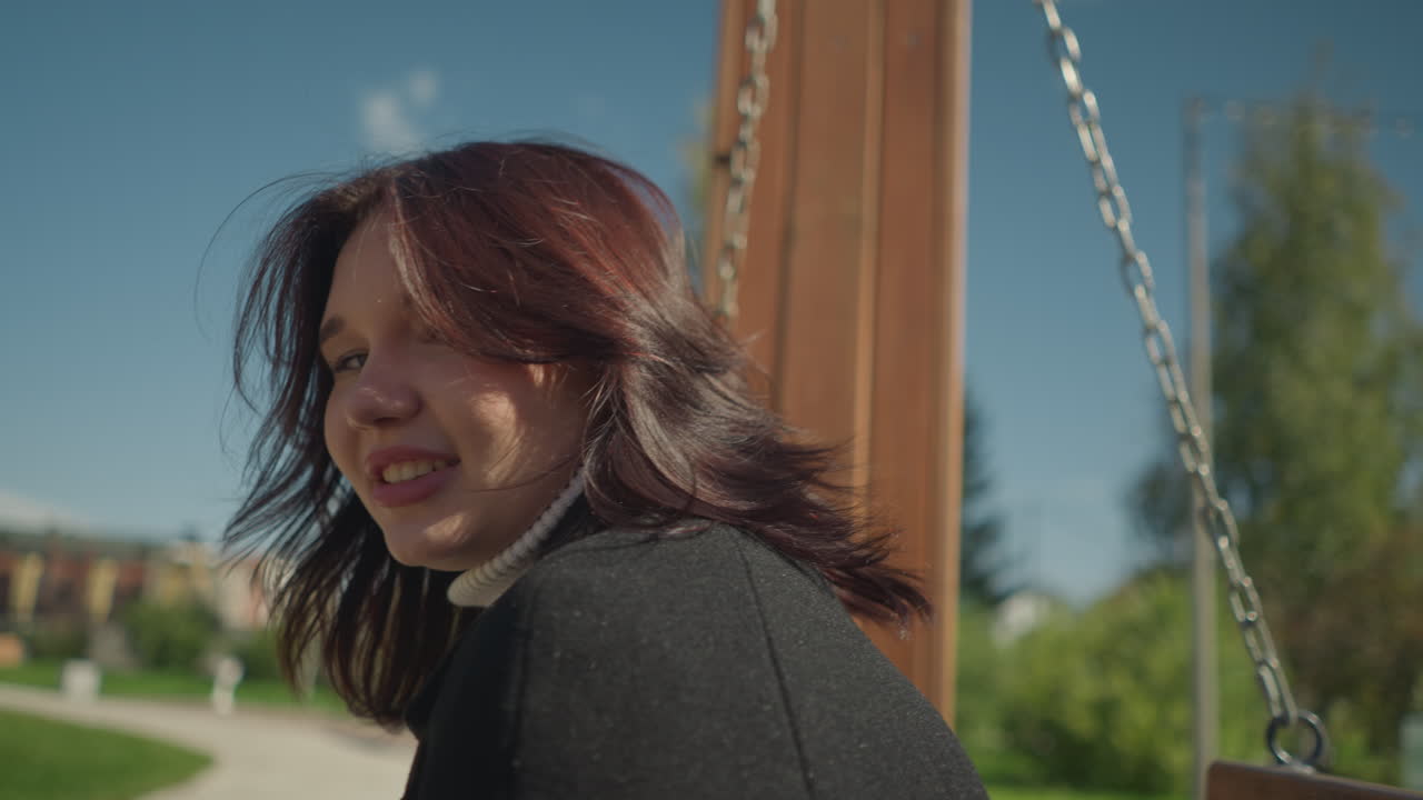 야외에서 흔들리는 동안 미소 짓는 젊은 여자의 클로즈업, 그녀의 머리카락은 부드럽게 바람에 흔들리고, 초록색과 이 있는 분위기로 둘러싸여 있습니다.