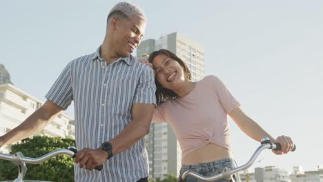 Feliz-Pareja-Birracial-Caminando-Con-Bicicletas-En-El-Paseo-Marítimo,-En-Cámara-Lenta