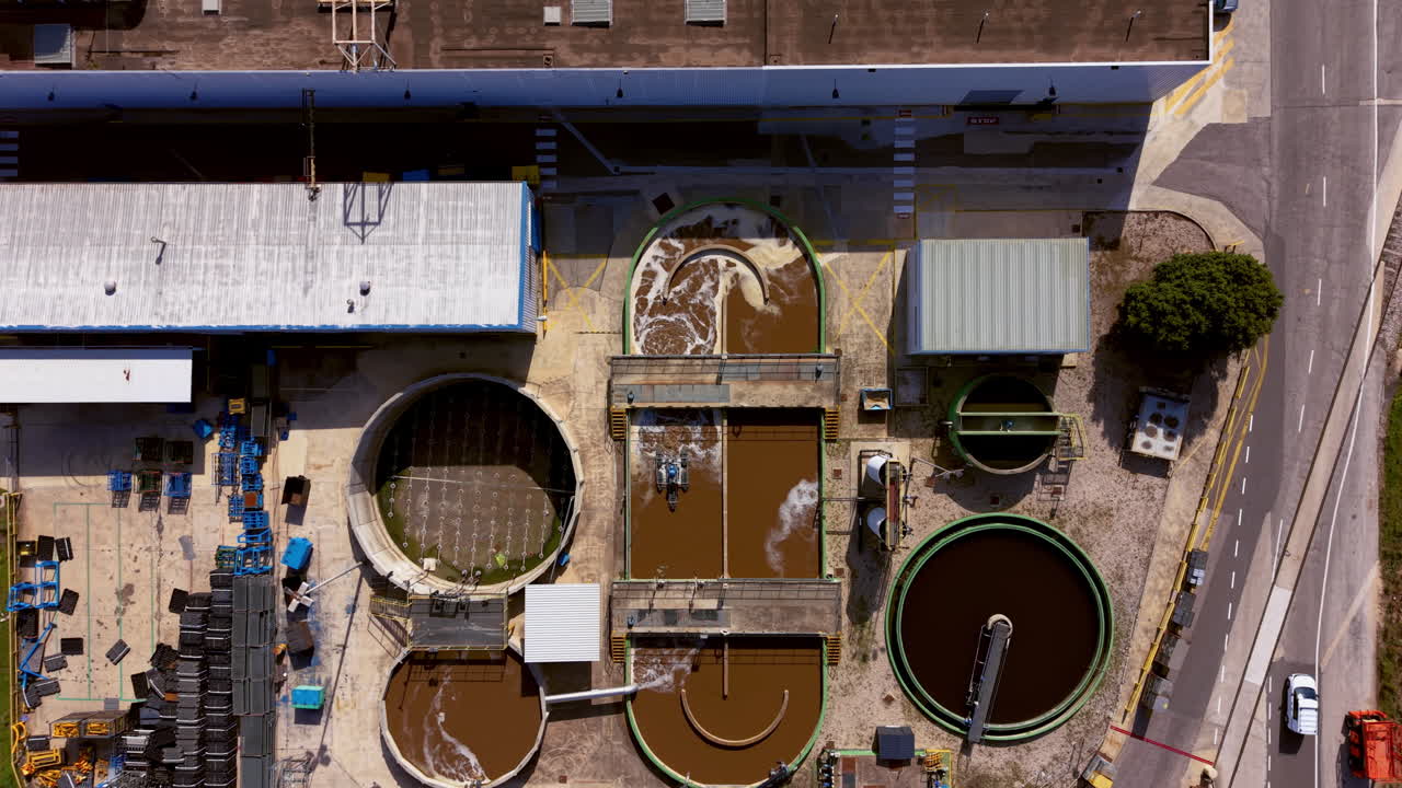 Overhead view of an industrial water treatment plant with circular clarifier tanks, sedimentation basins, and aeration zones showing brown effluent