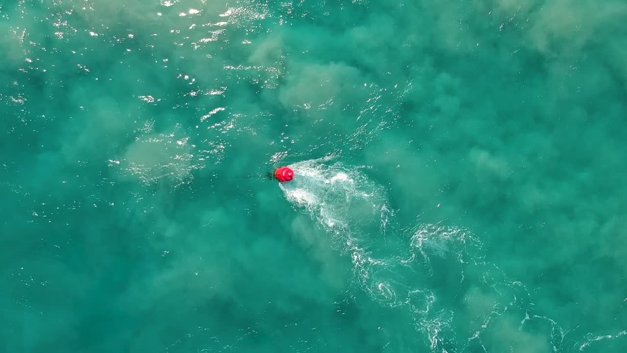 A marine navigational buoy swaying in a fast tidal current along a sandy section of water