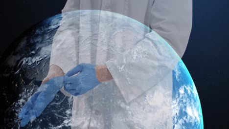 sección media de un médico que usa guantes quirúrgicos contra un globo girando sobre un fondo azul