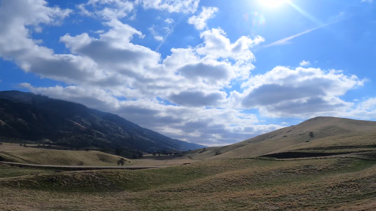 conduciendo a través de un paisaje pintoresco con colinas, árboles, prados en un hermoso día soleado con nubes esponjosas - punto de vista panorámico de la ventana del pasajero