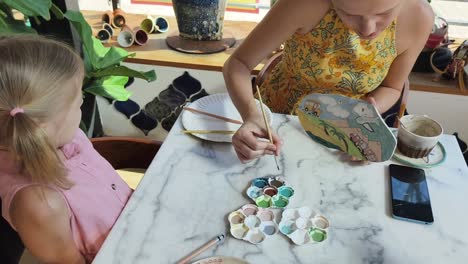 mother and daughter painting pottery at a cafe