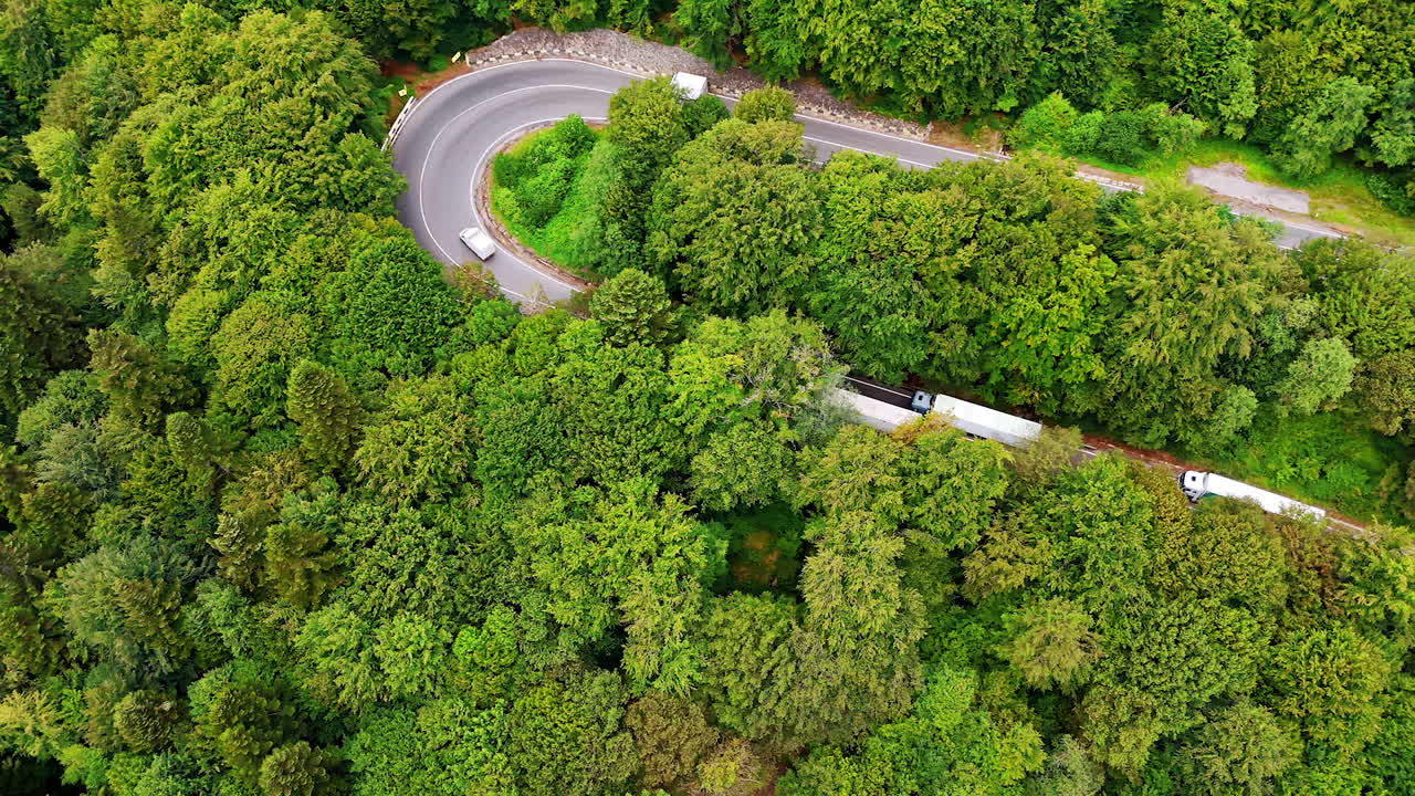 Mountain road winding through the Carpathians. Cars travel along a serpentine road cutting through lush green forests in the Romanian Carpathian Mountains