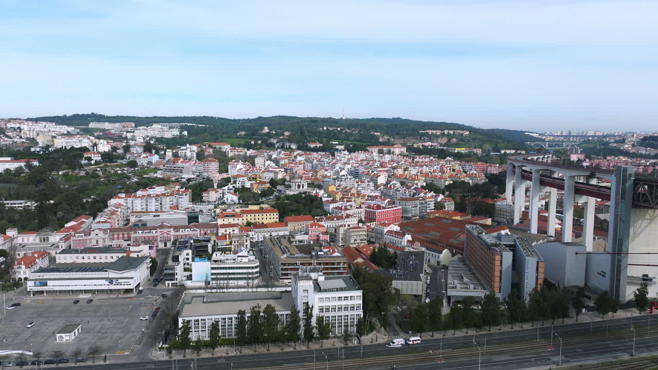 Cinematic aerial drone approach over the Lisbon cityscape on a bright morning, flying toward the Alcântara local area with Monsanto Park rising in the background