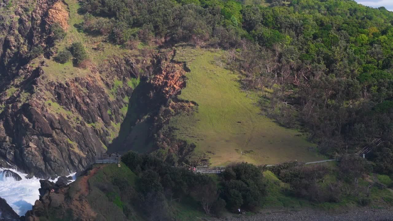 Aerial footage captures the rugged cliffs and lush greenery of Byron Bay, Australia, with waves crashing against the shore