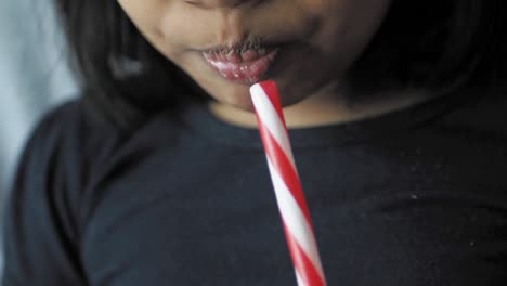 a young girl smiling while drinking from a red and white straw