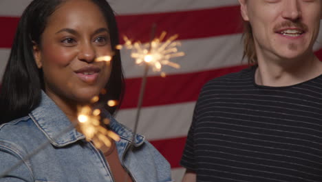 portrait en studio d'un groupe d'amis multiculturels tenant des feux d'artifice devant le drapeau américain célébrant le 4 juillet, jour de l'indépendance.