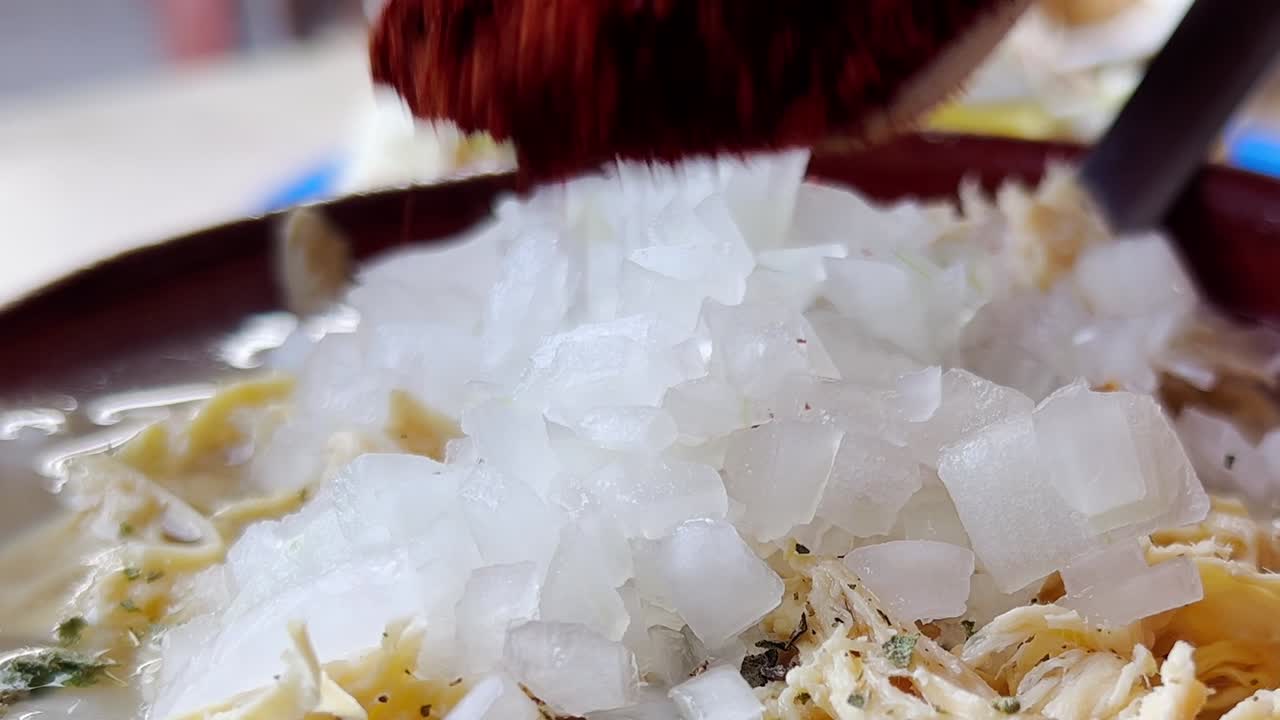 Close-up shot of chicken pozole topped with chopped onion