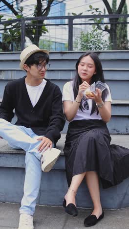 video vertical de una pareja asiática feliz comiendo comida callejera juntos en el parque