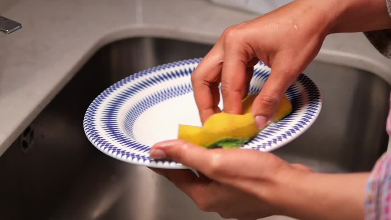 Primer plano de manos lavando un plato con una esponja en un fregadero de cocina.