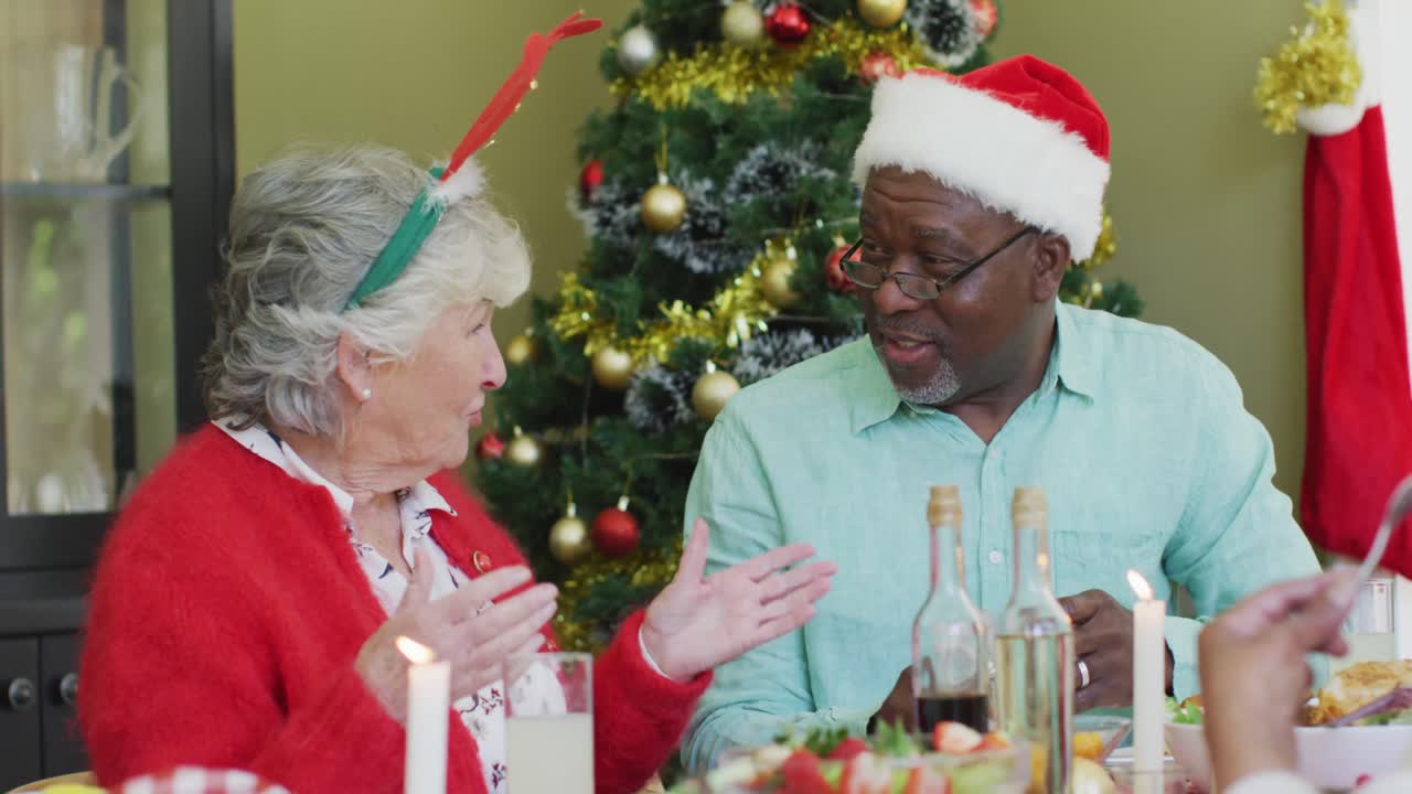 feliz pareja de ancianos diversos en sombreros de santa hablando en la mesa de la cena de navidad en casa