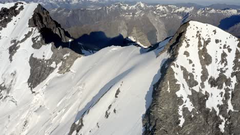 Huge-mountain-with-rock-and-snow-on-the-peak-amongst-a-spectacular-mountain-range-high-above-the-valleys-in-New-Zealand-during-sunrise