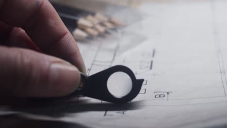 Hand-with-magnifying-glass-carefully-examines-construction-plans