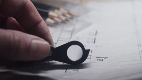 hand with magnifying glass carefully examines construction plans