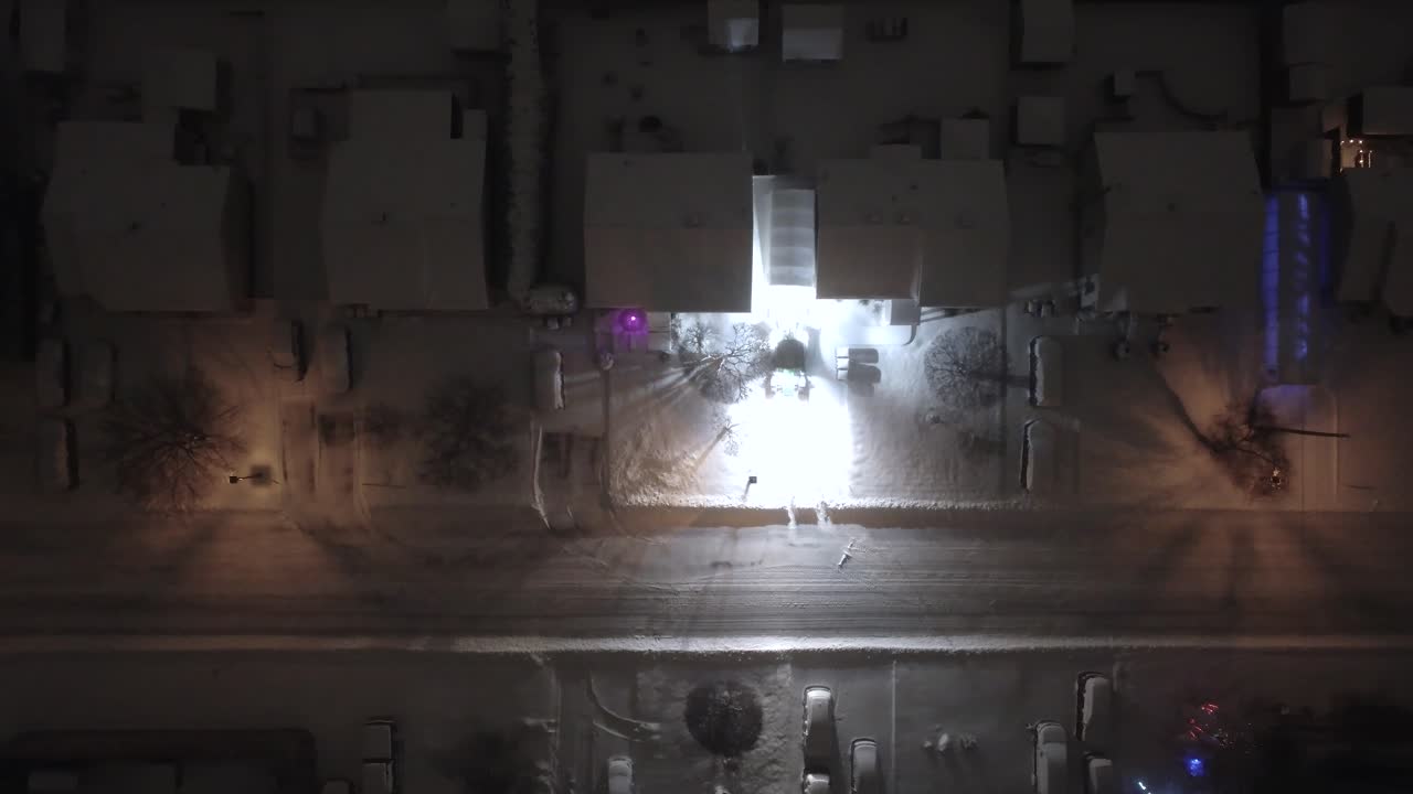 A tractor moves mthodically clearing fresh snow from a suburban driveway at night